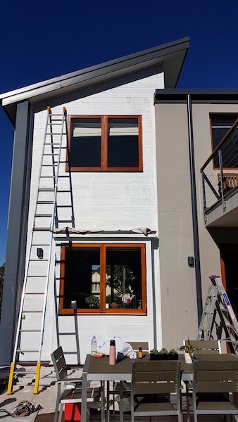 Outside view of 2 storey home that is about to be freshly painted in grey with dark blue trim.