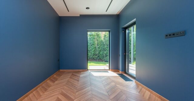 Modern interior with blue painted walls, chevron wood flooring, and large glass doors leading to a lush green backyard — contemporary home design inspiration.