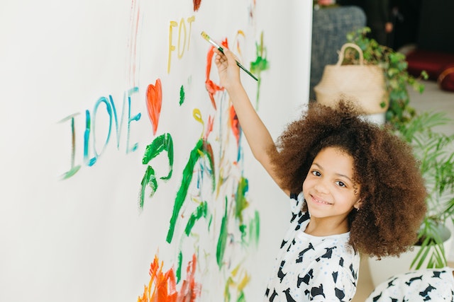 A child is happily painting on a white wall.