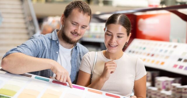 A man and woman smiling while selecting color samples from a display board in a home improvement store.