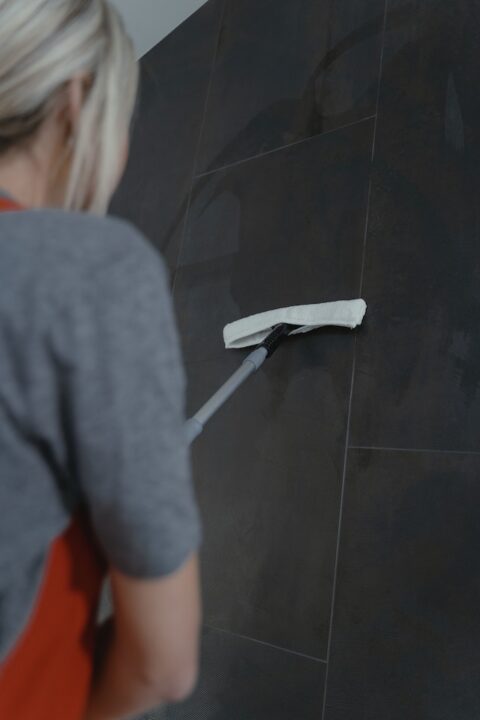 A person cleaning a gray wall thoroughly.