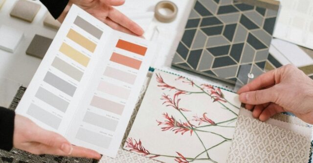 Two people are coordinating interior design elements, examining color swatches and fabric samples on a table filled with design tools and materials.
