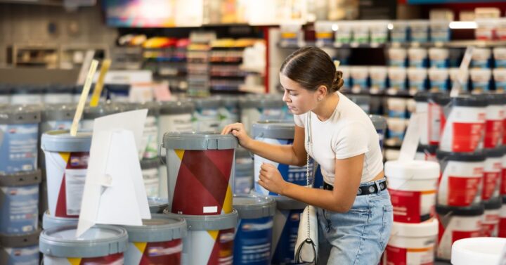Woman examining large paint buckets while shopping in a hardware store paint section.