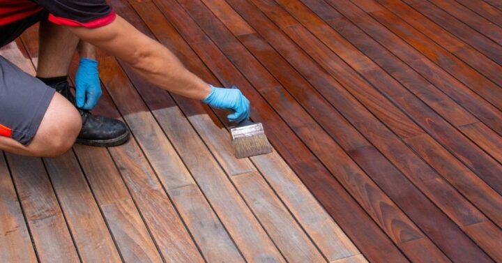 Worker applying terrace oil with a brush during deck renovation.
