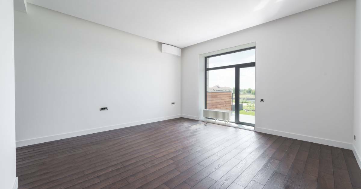An empty room with white walls and brown wooden floors.