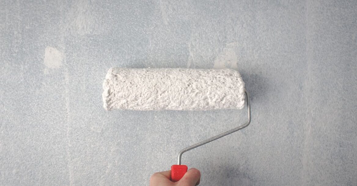 A roller brush is used to apply white paint on a wall.