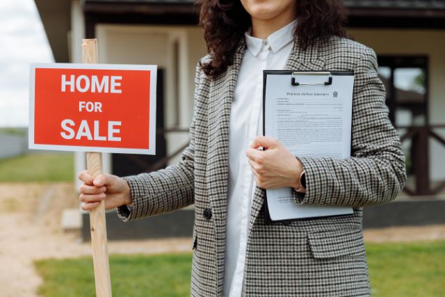 Close up photo of a woman holding a Home for Sale sign.
