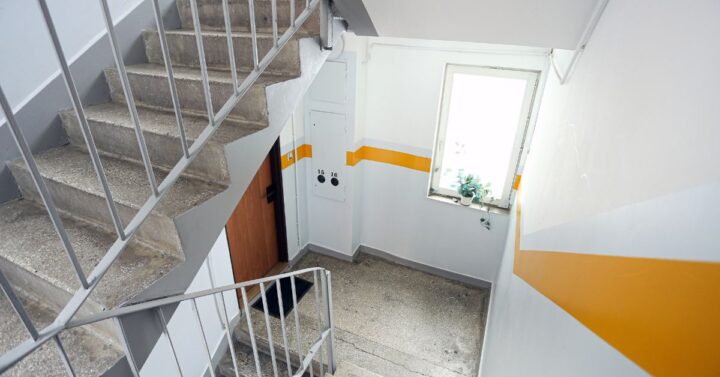 Concrete stairwell with metal railings, white walls, and a yellow stripe in a residential apartment building.