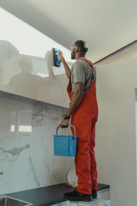 A man brushing a wall while holding a small pail.