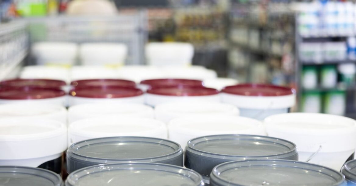 Paint cans and buckets displayed on store shelves in a home improvement retail aisle.