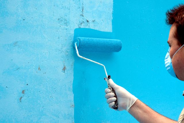A painter wearing a mask while painting a wall to avoid fumes.