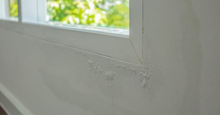Close-up of peeling and bubbling paint beneath a window frame, showing moisture damage on an interior wall.