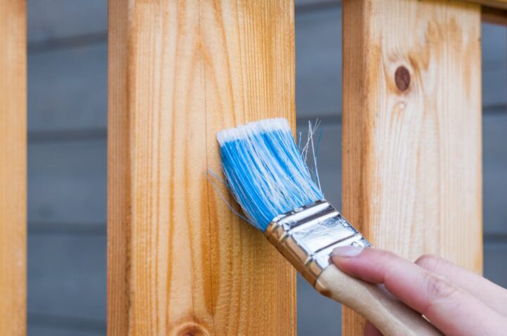 Person Holding Paintbrush to Paint a Fence.