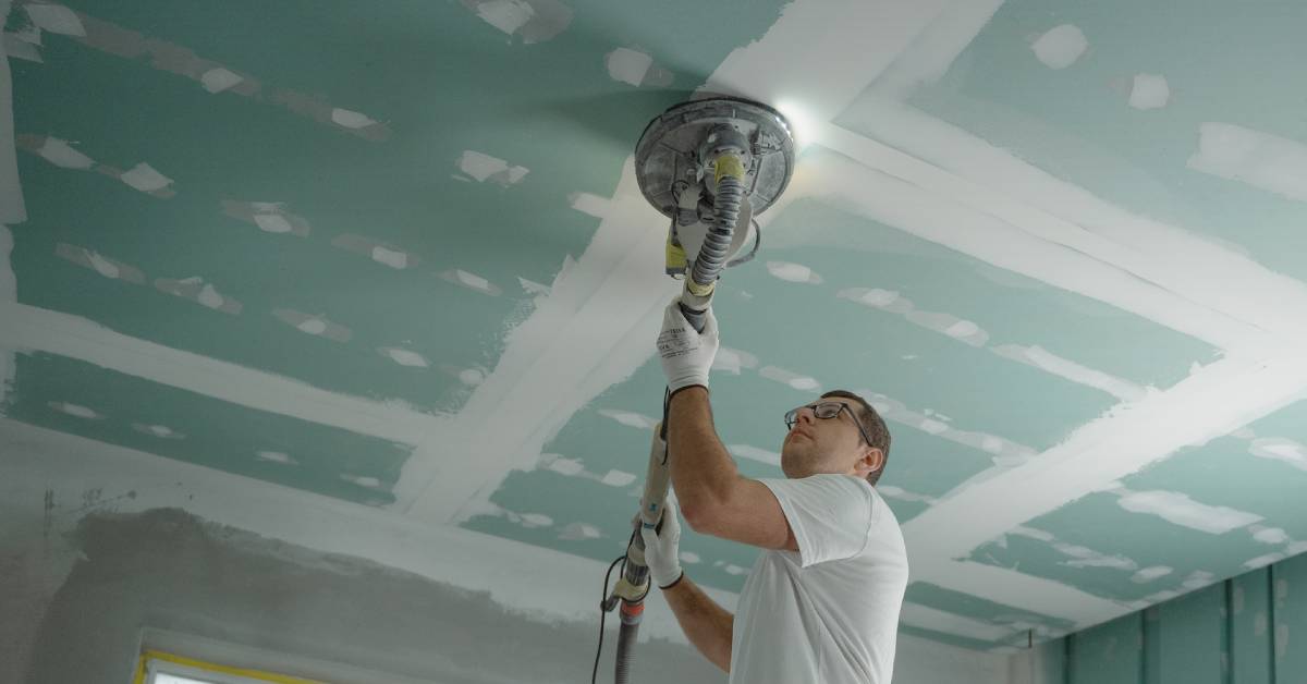 A man preparing and polishing the ceiling before painting.