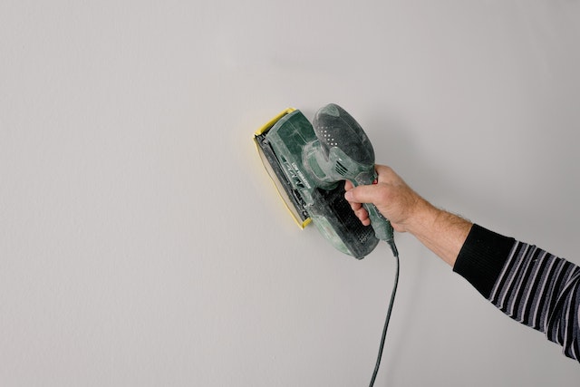 Professional painter polishing wall with construction tool.