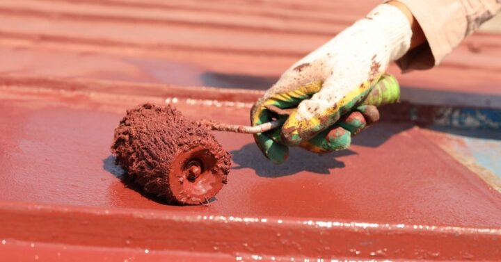 Painting an old metal roof with a roller.