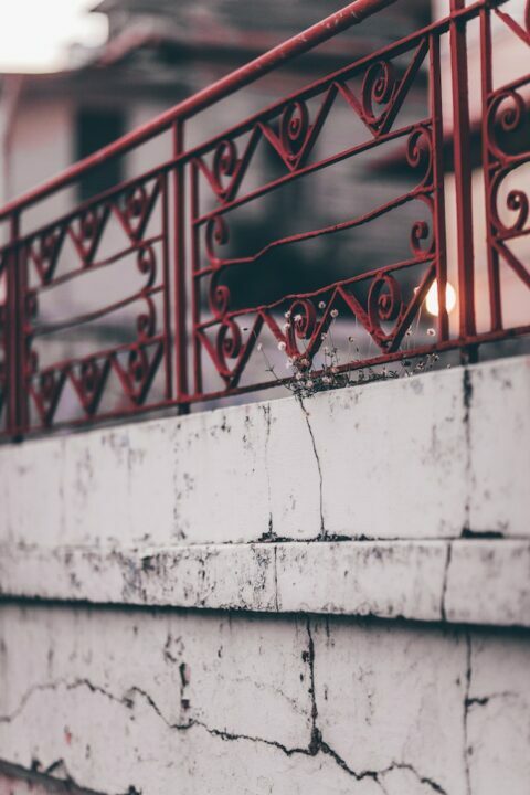 Rusty red fence on a cracked white wall.