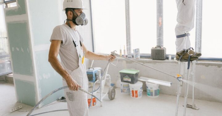 Man in White T-shirt Wearing Hard Hat Using a spray painting method.