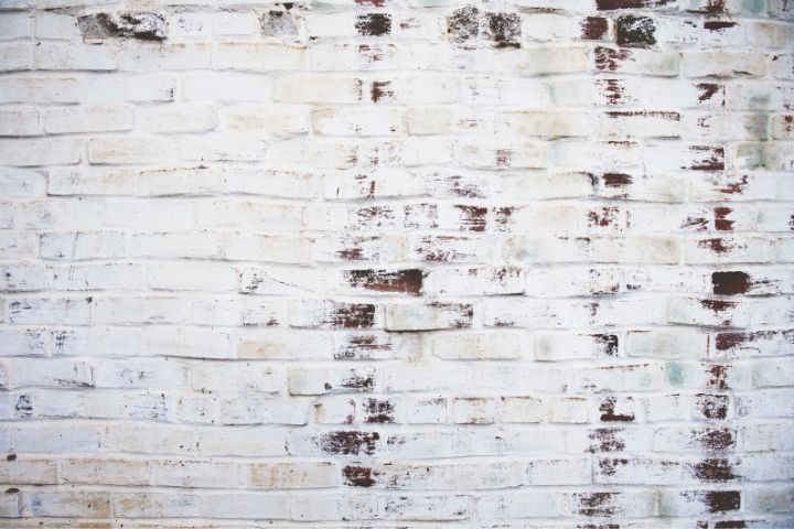Distressed white painted brick wall with uneven coverage and exposed red patches, perfect for vintage, shabby chic, or industrial-themed backgrounds.