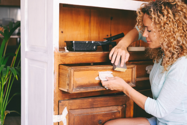 Woman preparing a cabinet for upcycling by sanding it.