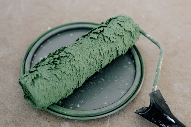 A used roller covered in green paint while sitting on top of a paint can lid.