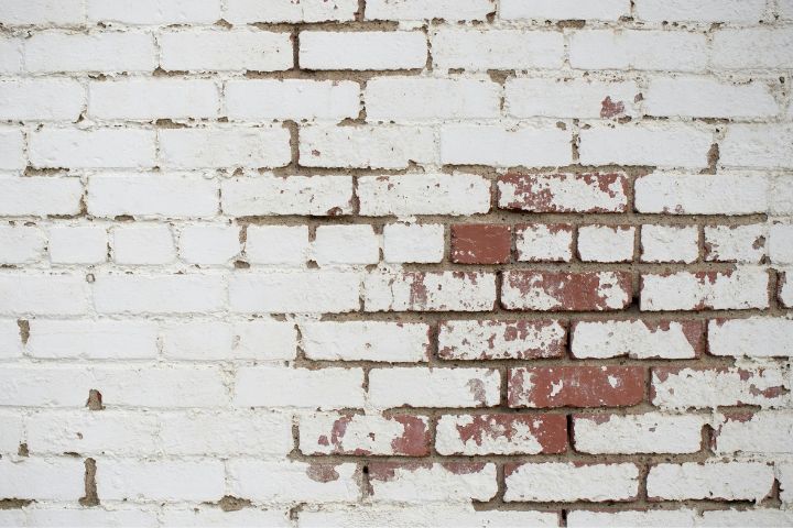 Whitewashed brick wall with peeling paint revealing red bricks underneath, showcasing a rustic and weathered texture ideal for vintage or industrial design themes.