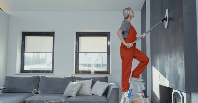 A woman on a ladder cleaning a wall using a mop.