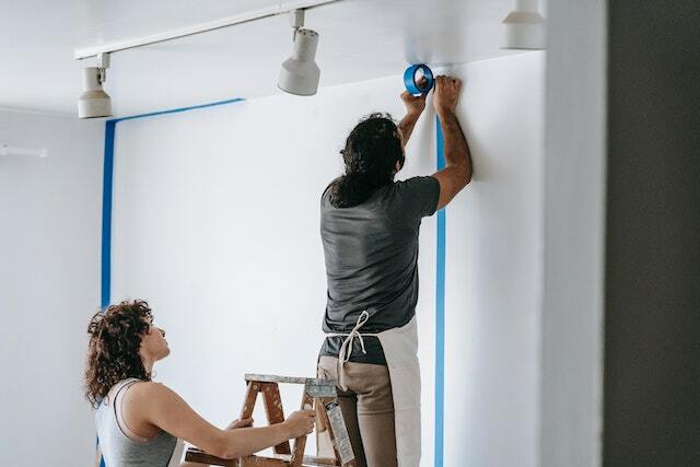 A couple doing DIY wall painting and applying painter's tape first.