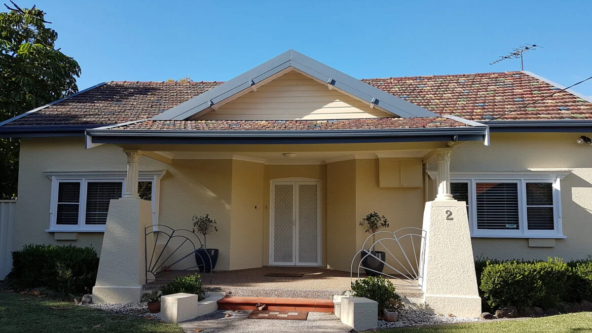 Single storey house exterior freshly painted in cream with blue guttering and trim.,