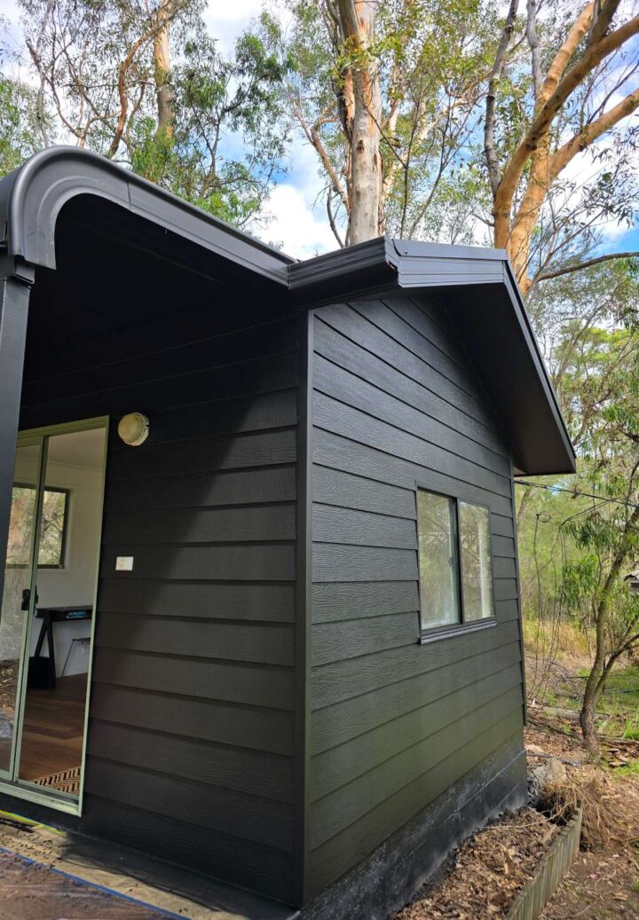 A close-up side view of a black-painted cabin with fresh cladding, showing a small window and clean roofline.