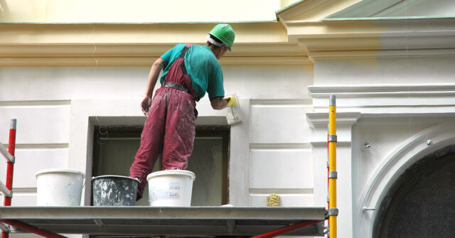 Painter standing on scaffolding to access high part of building.