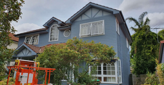 Freshly painted blue two-story timber house with sissor lift.