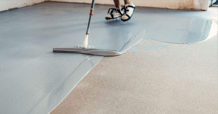 Worker applying thick floor coating with spongy rake to smooth it out