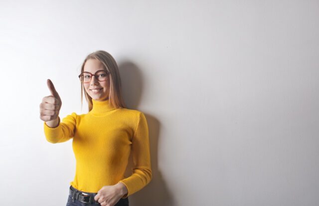 A girl wearing a yellow shirt showing a thumbs up for the freshly painted wall behind her.