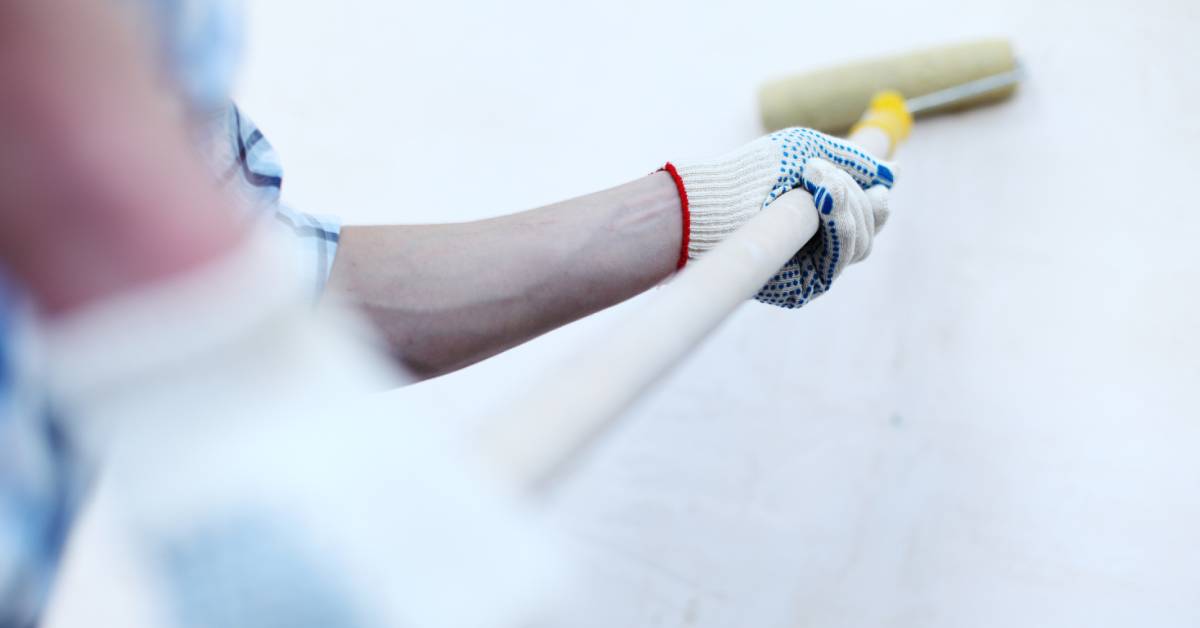 A man holding a paint roller is painting the house wall.