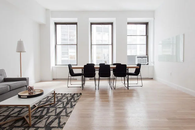 Large white room with dining room table and chairs, with three large windows on the back wall.