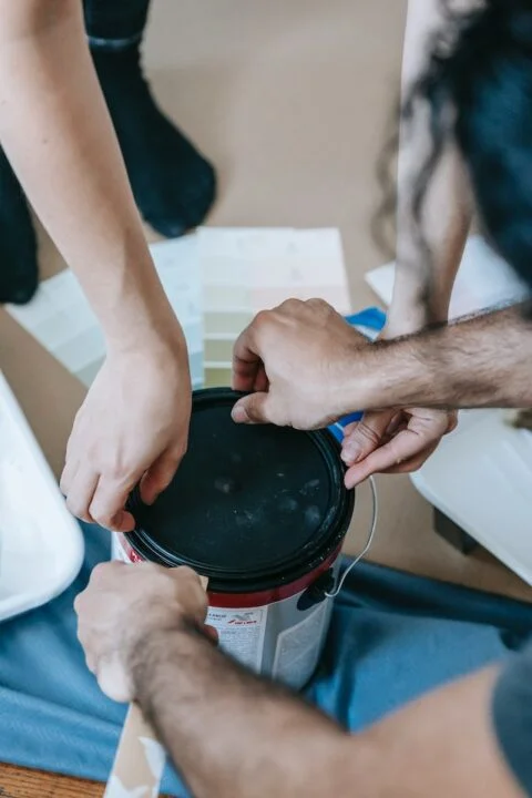 Two men opening a new paint can.