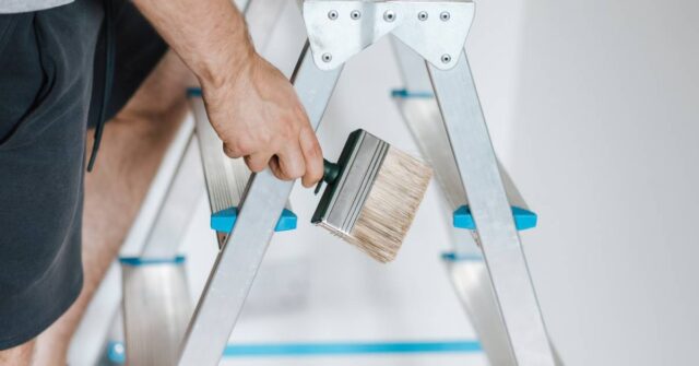 Man holding a painting while climbing on a ladder.