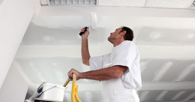 Painter painting ceiling white with roller.