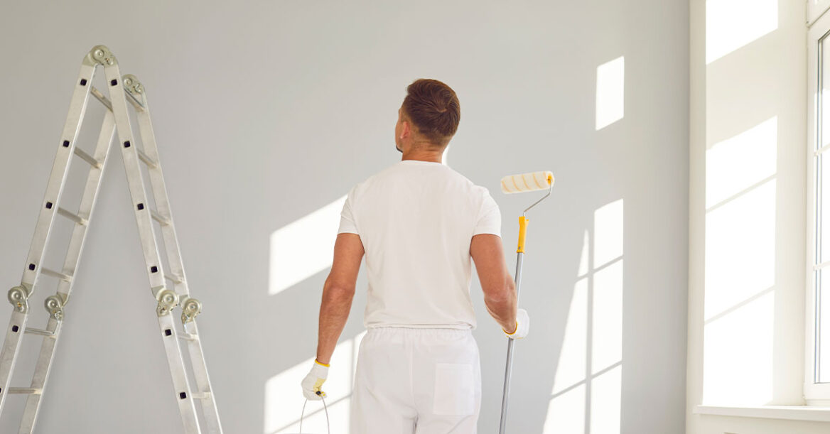 Painter with paint roller and paint can doing a touch up coat in a wall.