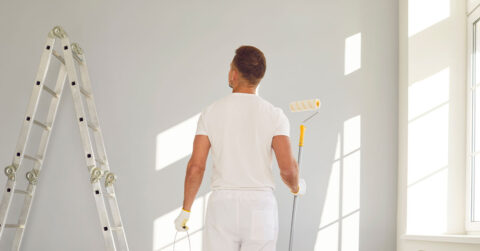 Painter with paint roller and paint can doing a touch up coat in a wall.