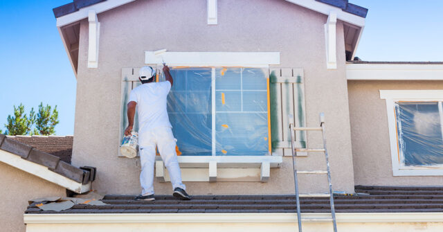 Experienced painter on roof painting around the external trim on a window.