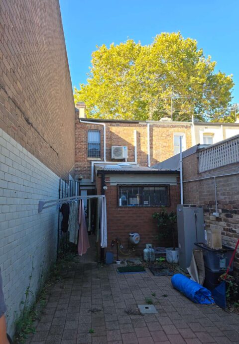 Rear courtyard of a terrace house with red brick walls and cluttered outdoor area; clothes drying on a line.