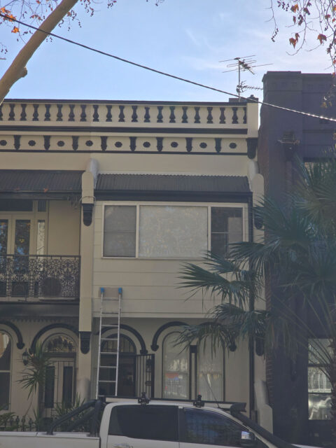 Two-story terrace house with classic architectural details, light brown exterior, and large front windows above an arched doorway. All freshly painted.