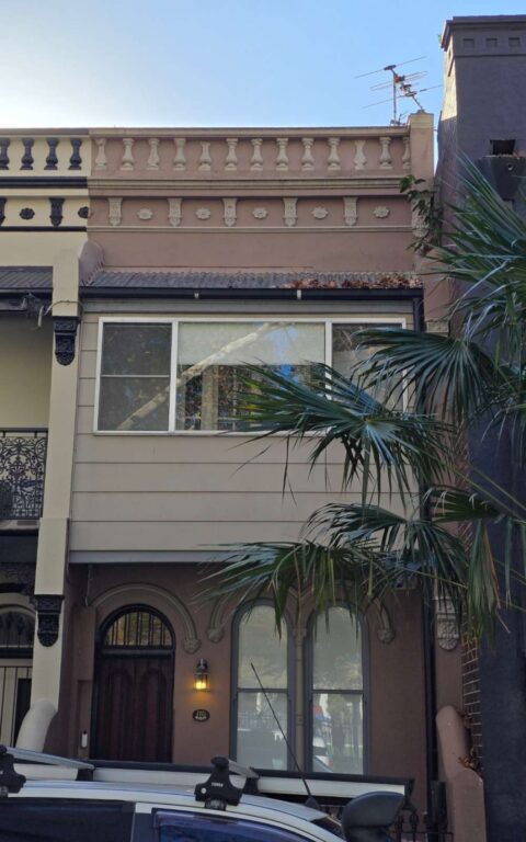 Two-story terrace house with classic architectural details, light brown exterior, and large front windows above an arched doorway.