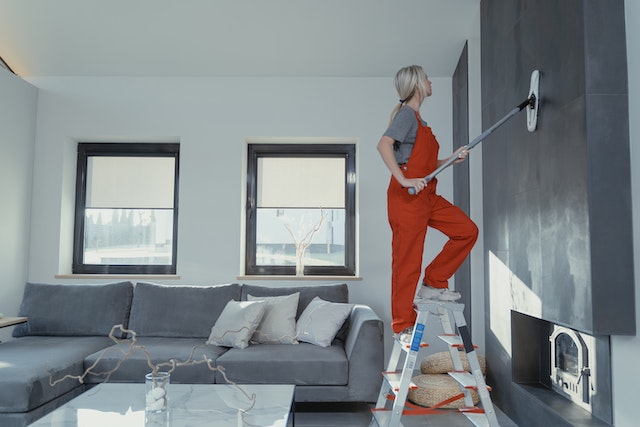 A girl cleaning andd wiping a wall using a mop.