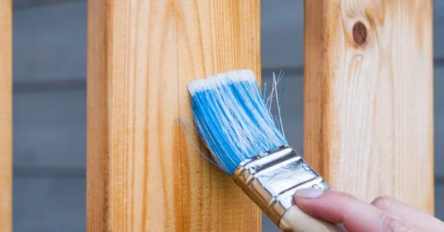 A man varnishing some wooden fence of a house.